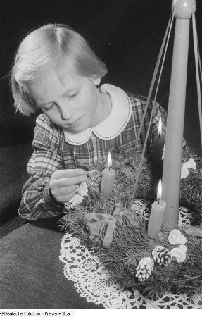 Ein Mädchen bein Entzünden der Kerzen eines Adventskranzes