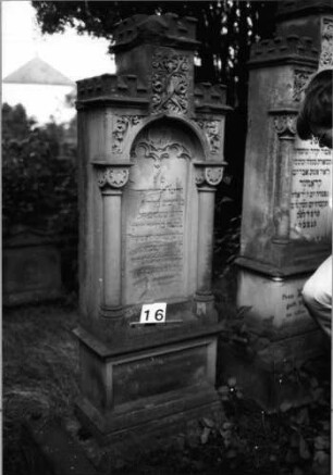 Grabstein 16 (Index: 99804463) Material: Sandstein Zustand: stark verwittert und abgeblättert Maße HxBxT: 176x63x32 cm Beschreibung: ädikulaartige Stele mit Halbsäulen, getreppter Sockel, Abschluß mit Zinnenaufsatz, Schriftfeld mit Maßwerk Symbolik: stilisierte Blätter, Maßwerk Besonderheit: kulturhistorisch wertvoll / künstl.-formale Gründe (Ornamentik, Form): Grabstein 16