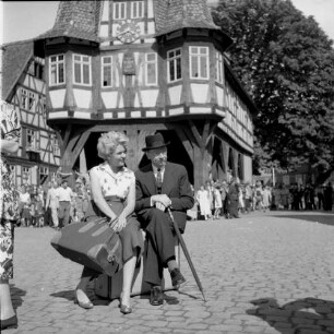 Michelstadt (Odenwaldkreis). Marktplatz. Filmaufnahmen. Szene mit wartenden Reisenden, auf Gepäck sitzend. Im Hintergrund Rathaus (Teilansicht)