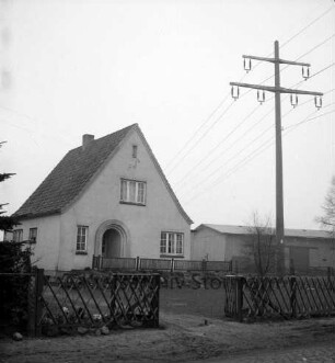 Überlandleitung: Starkstrommast neben Wohnhaus: vorn Tanne und Gartenzaun: hinten rechts Wirtschaftsgebäude