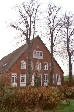 Klein Wesenberg (11): Bauernhaus aus Backstein: Giebelseite Wohntrakt mit Eingangstür, Sprossenfenstern, oben Bogenfenstern, mit Faschen: davor Bäume