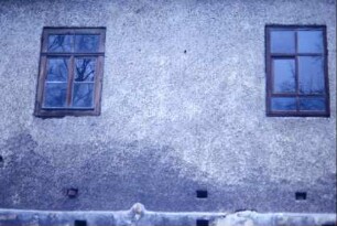zwei Sprossenfenster in einer Hauswand, darunter Lüftungslöcher
