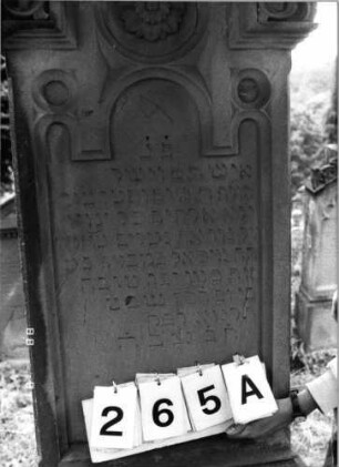 Grabstein 265 (Index: 100095781) Maße HxBxT: 189x57x23 cm Symbolik: Blumenkranz Besonderheit: kulturhistorisch wertvoll / hist.-wiss. Gründe (Gemeindestellung): Grabstein 265A
