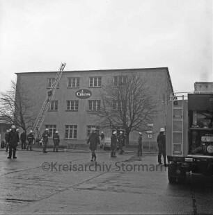 Brand: Gies Kerzen GmbH: Möllner Landstraße: Feuer in Parafinturm: rechts Löschfahrzeug: hinten Leiter an Firmengebäude: darauf Feuerwehrmann: vor dem Gebäude weitere Feuerwehrmänner und Wasserschläuche: rechts und links Bäume