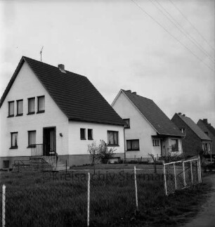 Neubausiedlung: Einfamilienhäuser mit Vorgärten: vorn mit Zaun abgetrennte Weide
