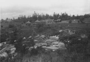 Engländersiedlung in Njombe : Eine Siedlung mit Häusern und Hütten an einem Wasserfall in Njombe.