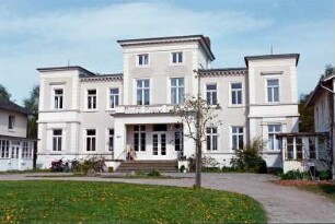 Gut Wulksfelde: ehemaliges Herrenhaus: Straßenfront mit Mittelrisalit, Freitreppe, Vorbau mit eingezogenem Eingangsportal, darüber Altan, zwei Eckrisaliten: beiderseits Kavalierhäuser [angeschnitten] mit verglasten Eingangsveranden: vorne Vorplatz, junger Baum, Auffahrt: 9. Mai 2003