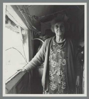 Alte Frau in Kittelschürze und Strickjacke am Fenster eines alten Gebäudes, Oppin