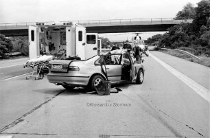 Bundesautobahn 1: bei Hammoor Richtung Norden: Verkehrsunfall: vorn Unfall-Pkw mit aufgeschnittenem Dach: links dahinter Rettungswagen mit geöffneten Türen und herausgezogener Trage, in der Mitte Rettungskräfte: im Hintergrund Mitte Rettungshubschrauber, Pkw und Brücke: 18. Mai 2000
