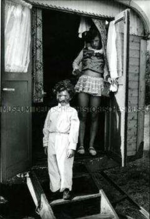 Zwei verkleidete Zirkuskinder am Eingang ihres Wohnwagens fotografiert (Altersgruppe 18-21)