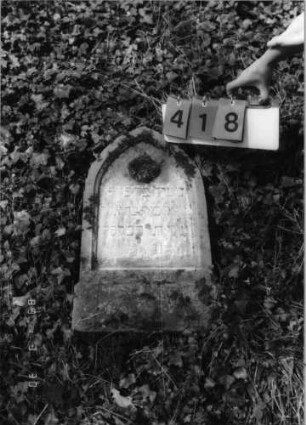 Grabstein 418 (Index: 99792031) Material: Sandstein Zustand: verwittert, Stele liegend Maße HxBxT: 64x37x16 cm Beschreibung: Stele, Spitzbogenabschluß, Schriftfeld eingetieft Symbolik: Blüte: Grabstein 418