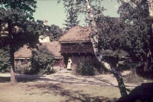 Reisefotos Skandinavien. Junge Frau in Tracht vor einem Holzhaus (vielleicht einer Räucherei)