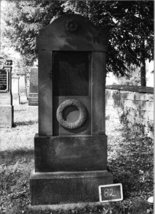 Grabstein 82 (Index: 99801928) Material: Sandstein mit Platte Zustand: ohne Inschrift Maße HxBxT: 200x72x36 cm Beschreibung: ädikulaartige Stele mit Pilastern, getreppter Sockel, Rundbogengiebel mit Gebälk Symbolik: Blüte, Kranz: Grabstein 82