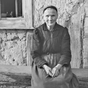 Strohgedecktes Blockhaus in Burg-Kauper. Frau Nowick in Spreewälder Alltagstracht vor ihrem Gehöft. : Ze słomu skryte kładźity twar statoka w Kupaŕskich Bórkowach. Knjeni Nowickowa we wšědnej Błótowskej drasće před swojim statokom.