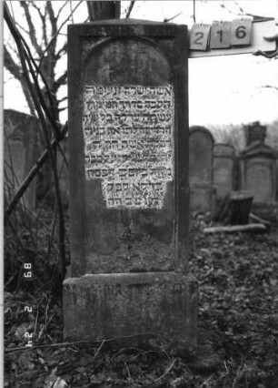 Grabstein 216 (Index: 99752103) Material: Sandstein Zustand: leicht verwittert Maße HxBxT: 144x47x25 cm Beschreibung: Stele, Sockel, obeliskenartiger Abschluß, Schriftfeld eingetieft m. Rundbogenabschlu Symbolik: Stern: Grabstein 216