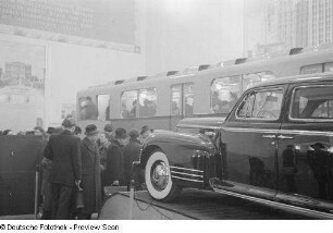 Besucher vor einem Automobil, im Hintergrund ein Triebwagen