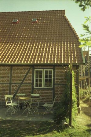 Benstaben 11: traufständige Fachwerkkate mit Ziegeldach: rückwärtige Traufseite, Teilansicht: Fenster: auf Terrasse Sitzgruppe: rechts an Giebelwand Gerüst