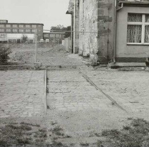 Kreuzung einer Werkstraße mit einem Anschlußgleis in ein (devastiertes) Fabrikgebäude