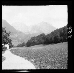 Unbekannte Gegend [Bayern?]: Weg in einem Tal mit bewaldeten Hügeln, im Hintergrund ein hohes Bergmassiv