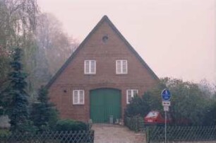 gegenüber Kirchenweg: giebelständiges Bauernhaus aus Backstein: Straßenfront mit Scheunentor: vorne Zufahrt, Jägerzaun