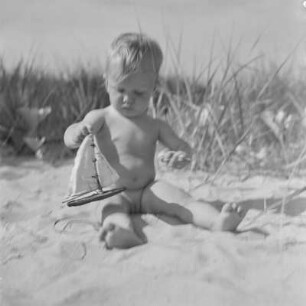 Kleinkind spielt mit einem Spielzeugboot am Strand