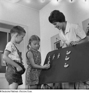 Zwei Kinder mit Erzieherin an einer Magnettafel, erste Mengenaufgaben lösend