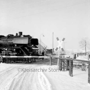 Bahnübergang bei Schrankenposten 60 mit vorbeifahrender Dampflokomotive: Bahnstrecke zwischen Hamburg und Lübeck: rechts Andreaskreuz: Winter
