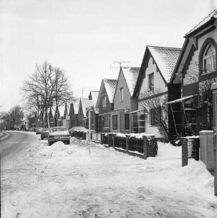 Pölitzer Weg: rechts eine Reihe von Einfamilienhäuser mit Vorgärten: davor parkende Pkws: hinten Bäume: Winter