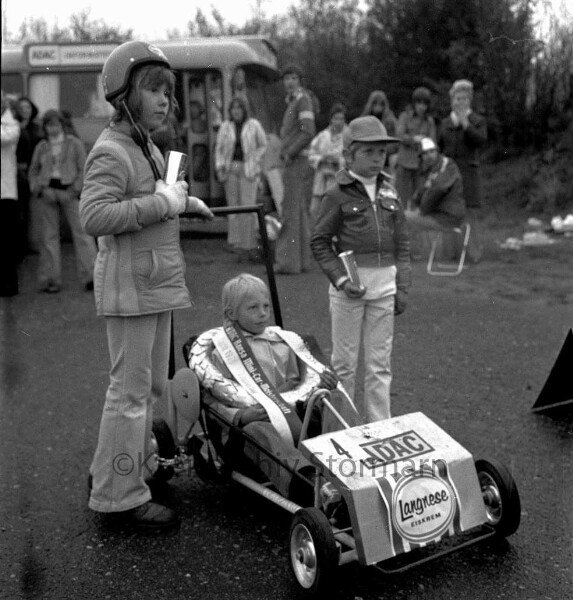 1. ADAC Hansa Mini-Car-Meisterschaft für Kinder: Veranstalter Allgemeiner Deutscher Automobil-Club e. V. ADAC: Travering an der Sehmsdorfer Straße: Gewinner der Klasse A Jan Neddenien aus Barsbüttel mit Siegerkranz in Minicar, flankiert von zwei Kindern mit Pokalen: hinten Bus, Zuschauer, 27. April 1974