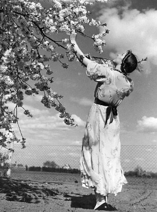 Käthchen im Mai. Junge Frau im Sommerkleid unter blühenden Zweigen