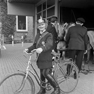 Tremsbüttel: Amtsfeuerwehrfest und 90-jähriges Jubiläum der Freiwilligen Feuerwehr Tremsbüttel: Jungfeuerwehrmann Olaf Tödt in historischer Uniform mit Feuerhorn und Fahrrad: im Hintergrund Feuerwehrgerätehaus, im Eingang zwei Feuerwehrmänner mit Pferdegespann