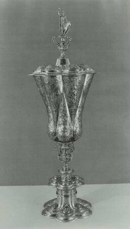 Hoher Pokal, sogenannter Ageleybecher (mit zwei Reihen von je 6 ineinandergreifenden Fischblasen und antikem Krieger mit Lanze und Schild als Krönung (im Inneren sechskantige hohe Spitze, wie in Nürnberg bei dem Meisterstück in Ageleybechern vorgeschrieben)