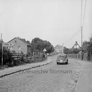 Im Seybek: Kreisstraße mit Kopfsteinpflaster Richtung Pölitz: links Hinweisschild: rechts VW-Käfer: hinten Wohnhäuser und Bauernhäuser
