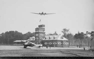 Blick vom Rollfeld auf Abfertigungsgebäude mit Kontrollturm, Verkehrsflugzeug Junkers G 24 (im Anflug) und Verkehrsflugzeug Junkers F 13 : Dresden. Flugplatz Dresden-Heller. Blick vom Rollfeld auf Abfertigungsgebäude mit Kontrollturm, Verkehrsflugzeug Junkers G 24 (im Anflug) und Verkehrsflugzeug Junkers F 13