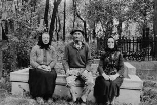 Zwei Frauen und ein Mann auf einem Friedhof