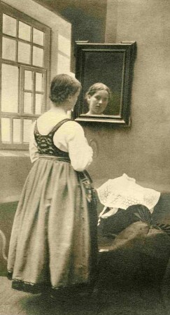 Mädchen in Volkstracht vor einem Spiegel nebst Fenster, rückseitig. Halbtotale