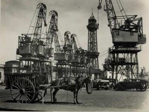 Barcelona. Spanien. Krane im Handelshafen. Im Vordergrund ein Pferdefuhrwerk. Rechts der gusseiserne Turm, Torre Jaume I. der Hafenseilbahn