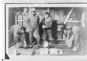 Vier Soldaten der Technischen Betriebe der 27. Infanteriedivision beim Metallgießen