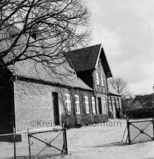 Volksschule: vorn Schulhof mit Zaun: rechts oben Baumäste