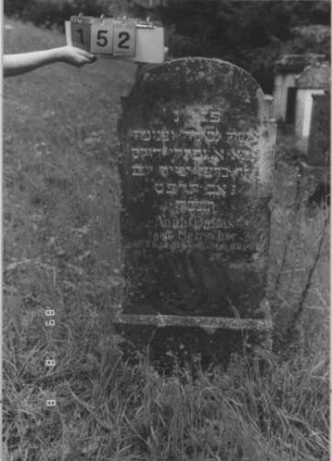 Grabstein 152 (Index: 99800199) Material: Granit Zustand: bewachsen Maße HxBxT: 126x54x16 cm Beschreibung: Stele, zweifach eingezogener Korbbogenabschluß, Sockel Symbolik: Davidstern: Grabstein 152