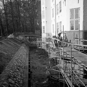 Restaurierung: Arbeiten an Fundament: Gerüst, Arbeiter: innerer Graben: neue Grabenversteifung mit Holzbohlen am Grabenfuß: hinten Arbeiter bei Befestigung der Grabenböschung mit den alten Findlingen: im Hintergrund kleine Parkbrücke über äußeren Schlossgraben