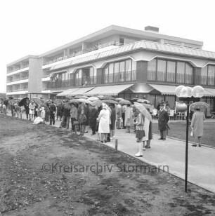 Seniorenwohnanlage Rosenhof I: Hoisdorfer Landstraße: Einweihung: Außenansicht des Gebäudekomplexes: davor Besucher mit Regenschirmen auf Weg