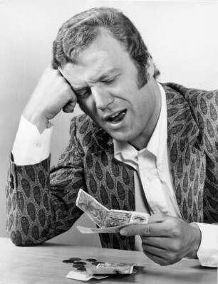 Ein Mann sitzt am Tisch und schaut auf sein Geld. Er fragt sich: "Wird es reichen?"