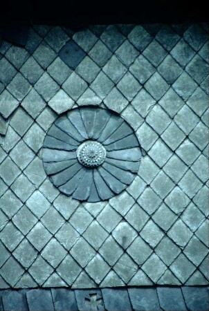 Detail einer Hauswand: Schieferrosette, darunter in einem Schieferstein ein Kreuz
