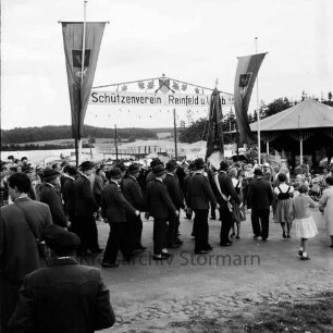 Schützenfest: Veranstalter Schützenverein Reinfeld und Umgebung von 1954 e.V.: Umzug: Ahrensböker Straße: Ankunft der Schützen mit Fahne am Festplatz: dahinter Torbogen mit Aufschrift "Schützenverein Reinfeld und Umgebung", beiderseits Fahnenschmuck: Karussells, Jahrmarktstände, Zuschauer, 30. August 1959