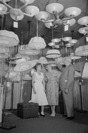 Drei Personen begutachten auf der Leipziger Herbstmesse 1955 ausgestellte Deckenlampen