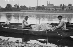 Meißen. Zwei Fischer, im Kahn sitzend, beim Ausbessern eines großen Netzes. Blick über die Elbe auf die Ofenfabrik