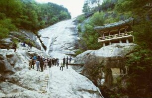 Reiseteilnehmer auf einem Felsen unterhalb eines Wasserfalls stehend