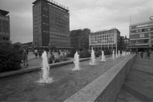 Essen: Gildenplatz [Kennedyplatz], Reihe von Springbrunnen im Vordergrund