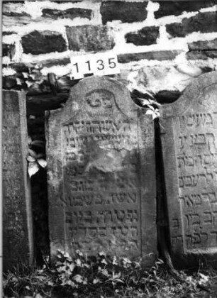 Grabstein 1135 (Index: 99630638) Material: Sandstein Zustand: stark abgeblättert mit Textverlust Maße HxBxT: 99x51x12 cm Beschreibung: Stele mit eingezogenem Segmentbogenabschluß, Schriftfeld eingetieft: Grabstein 1135